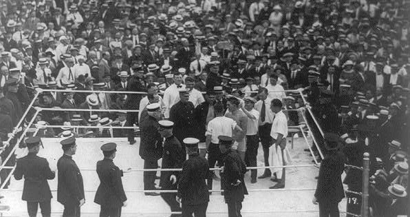 July 2, 1921. Jack Dempsey and Georges Carpentier get ready to square off in championship fight before 80,000 fans.  The fight ushered in a 'golden age' of sport in the 1920s, and with radio, the beginnings of sport as mass-audience, big-business entertainment.  