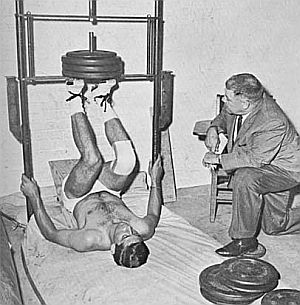 Joe Namath doing leg strength training while coach Weeb Ewbank looks on.