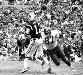 Joe Namath (12), about to take a hit from an oncoming Denver Bronco (87), October 13, 1968, a game in which Namath threw five interceptions.