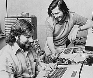 Steve Wozniak and Steve Jobs in their garage working with what appears to be an Apple II computer, likely in 1977.