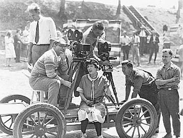 Allan Dwan, seated left, on a movie set in the silent film era with Gloria Swanson, center, possibly in the 1910s-1920s. Click for book on Allan Dwan.