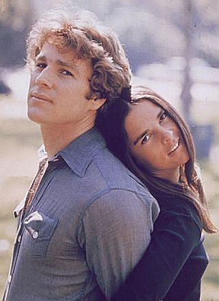 Ryan O’Neal and Ali MacGraw in 1970 studio photo: Harvard ice-hockey star & hot head meets wise-cracking Radcliffe beauty in popular novel & Hollywood film, “Love Story”. Click for film.