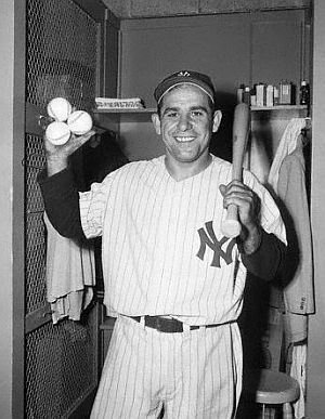 May 1955: Yogi Berra holding three baseballs and bat in clubhouse.