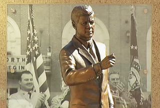 Another view of the JFK statue at the Fort Worth, Texas JFK tribute site at General Worth Square, downtown, set against large period photographs of the President’s 1963 visit.