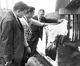 September 1964: Councilmen Edward F. Katalinas (left), Henry Sinkiewicz, and John Pilch examine oil-soaked white cloth dipped in the Cuyahoga. Photo, Cleveland Press.