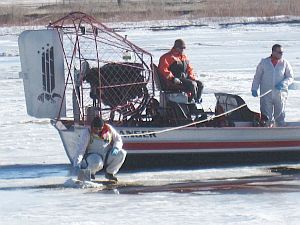 Oil spill crew in air boat on icy Yellowstone River have safety line tied to worker trying to soak up oil, January 2015.