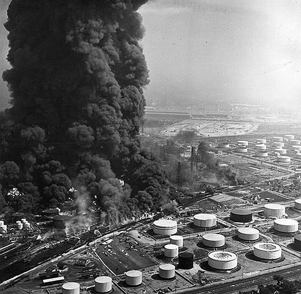 Aerial photograph of the spreading August 1955 oil refinery fire at Standard Oil’s Whiting, Indiana complex. The 8-day fire, set by a processing tower explosion, would consume at least 45 acres of storage tanks and damage nearby homes and businesses. Two people were killed, another 40 injured, and 1,500 evacuated.