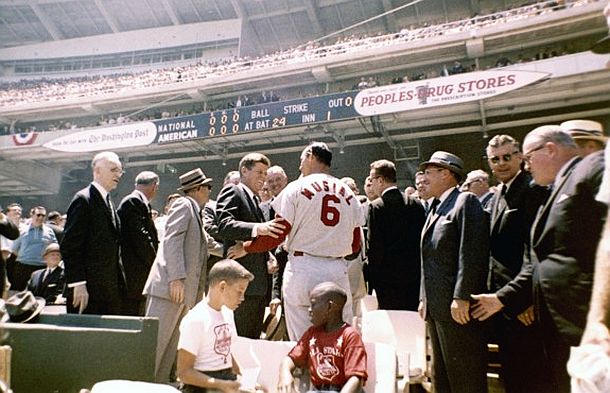 JFK and Stan Musial greeting one another at the 1962 All-Star game, played at Washington, D.C.’s new Washington Stadium. Among those in the President’s party that day were: Speaker of the House, John  McCormack, Kennedy aide, Dave Powers, Vice President Lyndon Johnson, Lawrence O’Brien, Commissioner of Baseball, Ford Frick, and in the foreground, center, two young guests of the President from the Washington Boys Club. Click for framed, Musial-autographed, 16x20 commemorative photo.