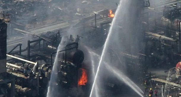 March 23, 2005: BP’s Texas City, Texas oil refinery continues to burn in some areas following the explosion there, as water is trained on remaining fires and hot spots.  Note emergency response workers, yellow hats, lower right.