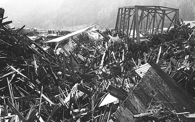 Crowd of onlookers in the distance surveys the enormous debris field jammed up against a downstream bridge following the Buffalo Creek coal flood. Some survivors reported homes exploding or splintering apart with the wave's impact. Gazette-Mail/L. Pierce.