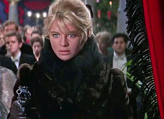 Lara, with gun, shoots at Komarovsky during Christmas party as he is playing cards in the rear of the hall.