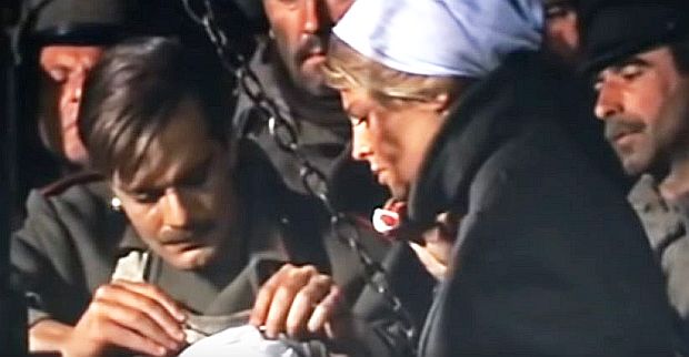 On the back of their hospital wagon, on a makeshift operating surface, Zhivago is at work on a wounded soldier as nurse Lara assists in dabbing the wound with swab.